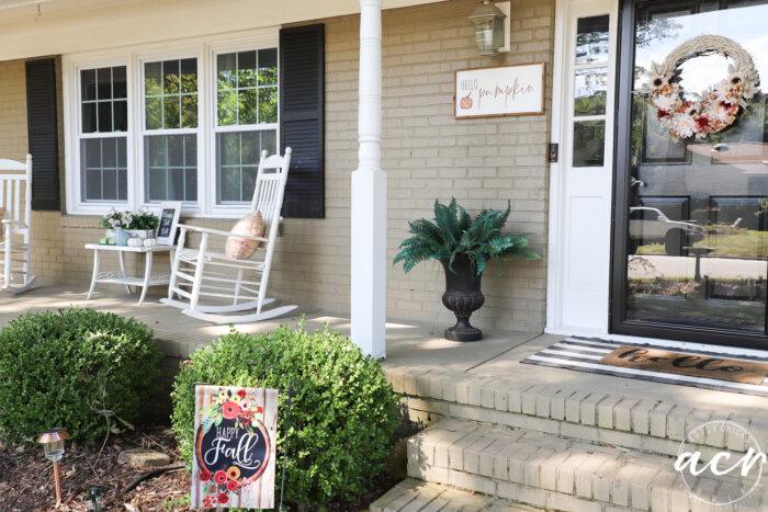 front porch with white rockers, fall flag, front door with wreath