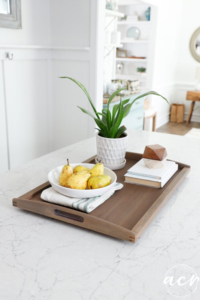 wood tray on island with green plant and bowl fruit