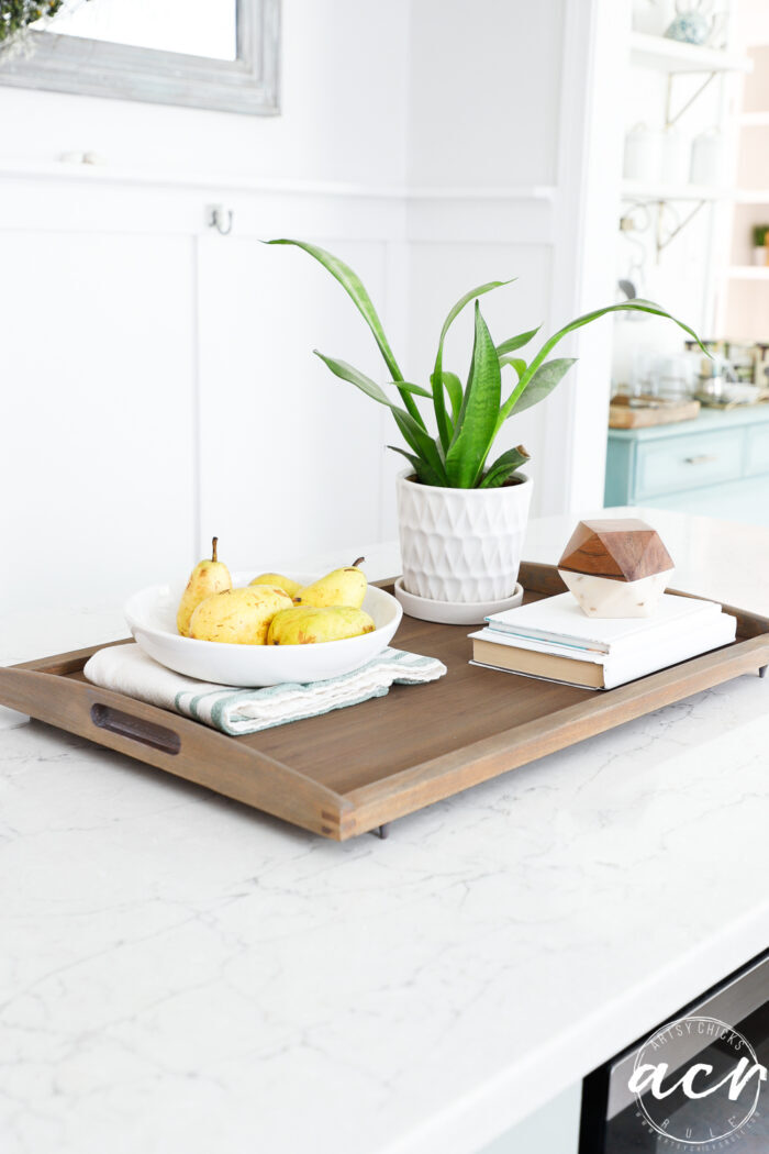 wood tray on kitchen island with fruit in bowl and green plant