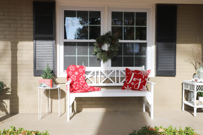 white bench on porch with red blanket green wreath on window