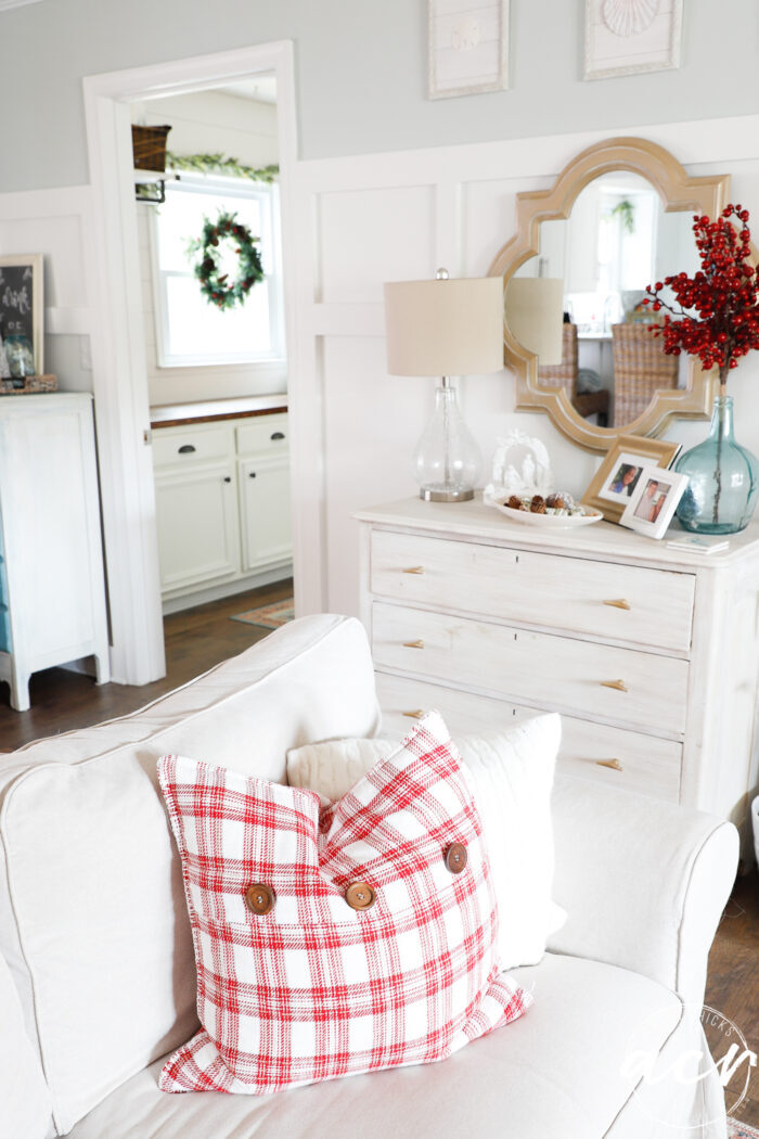 couch with white pillow, red pillow and white dresser behind decorated for the holidays