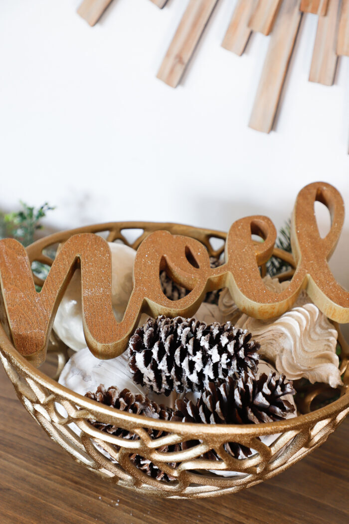 gold bowl with pines cones and a wood noel figure