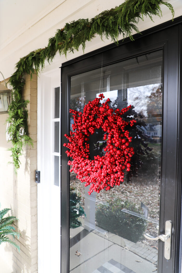 front door black with greenery above and red berry wreath on door