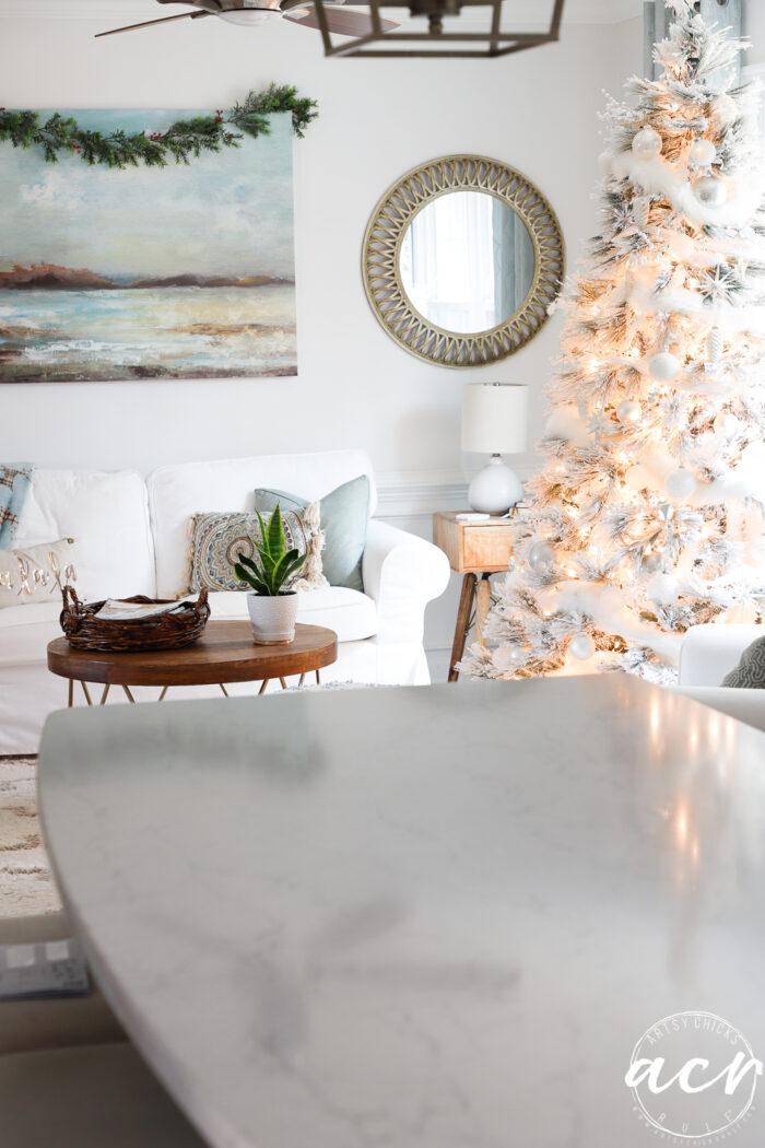 kitchen island with white christmas tree in other room behind