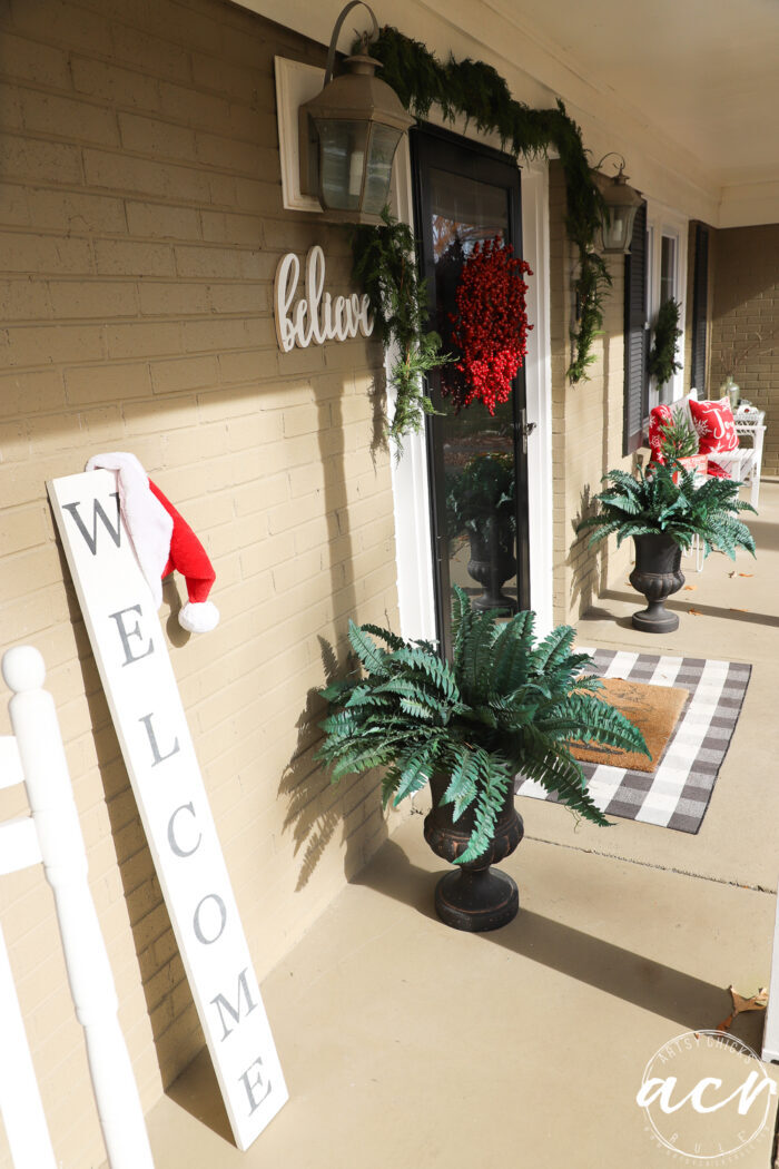 looking down the porch with welcome sign, welcome mat, greenery and red accents