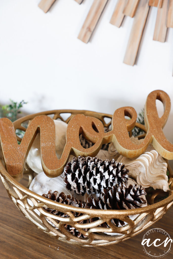 gold bowl with pines cones and a wood noel figure