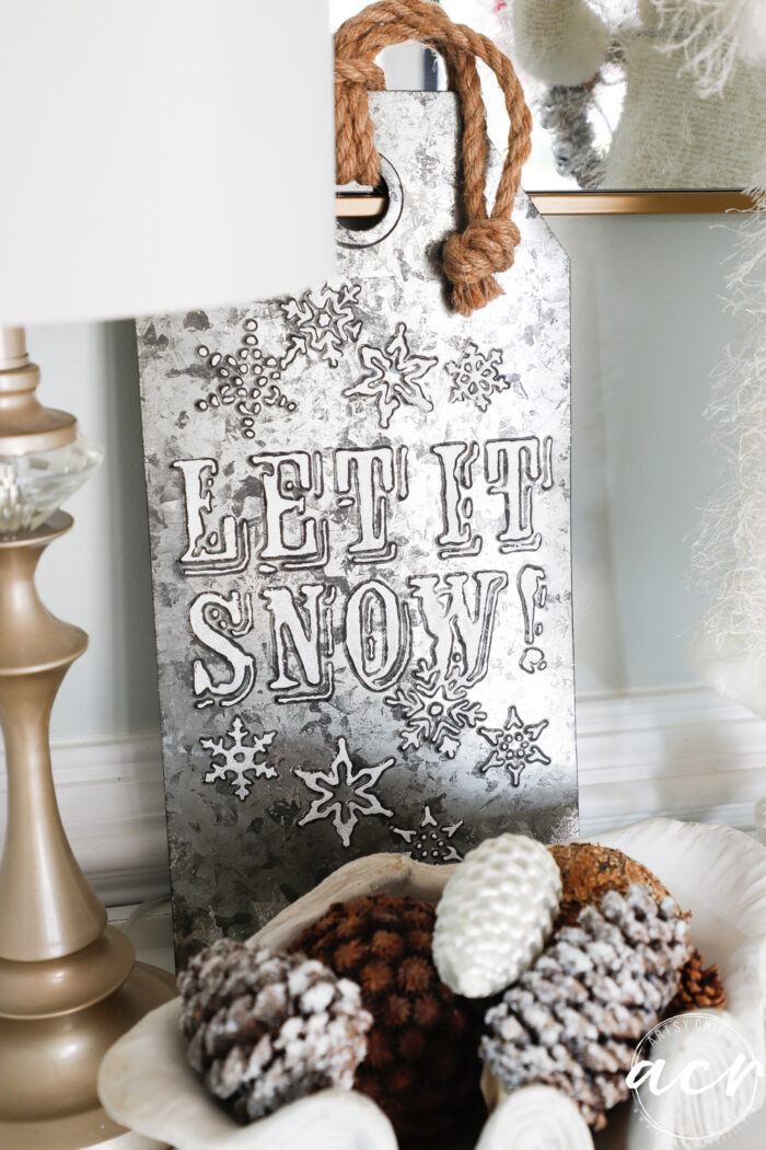let it snow metal sign with bowl of pine cones on foyer table