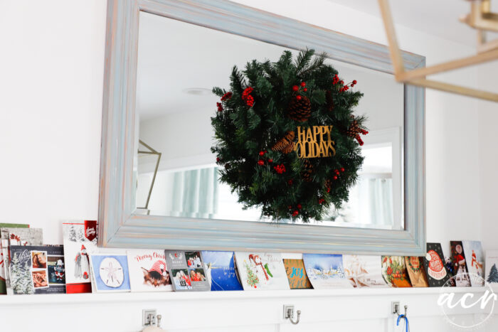 mirror on wall with green wreath and christmas cards all along the ledge below