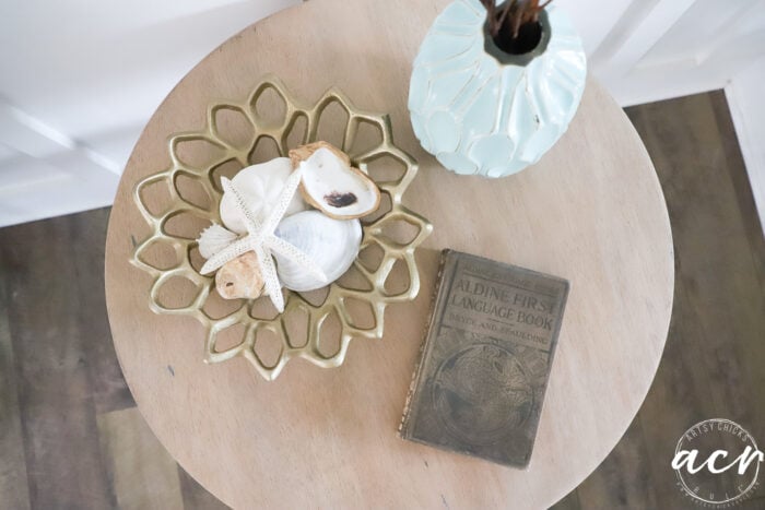 top view of table styled wtih old book, gold bowl and aqua vase