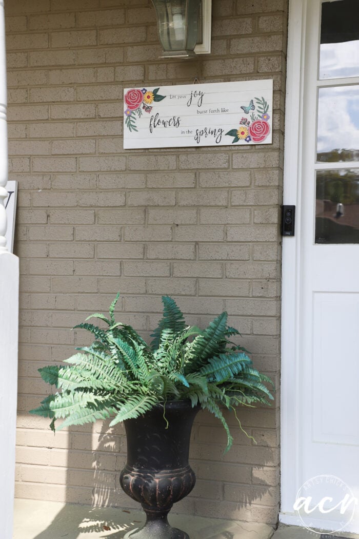 spring sign hanging on porch with green fern