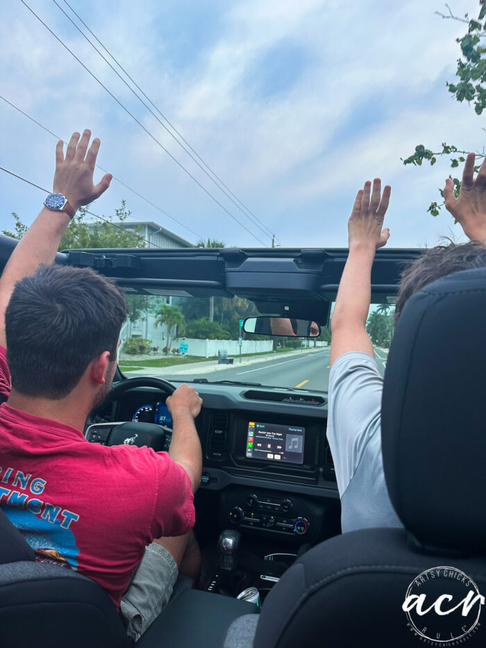 two men driving convertible with hands up
