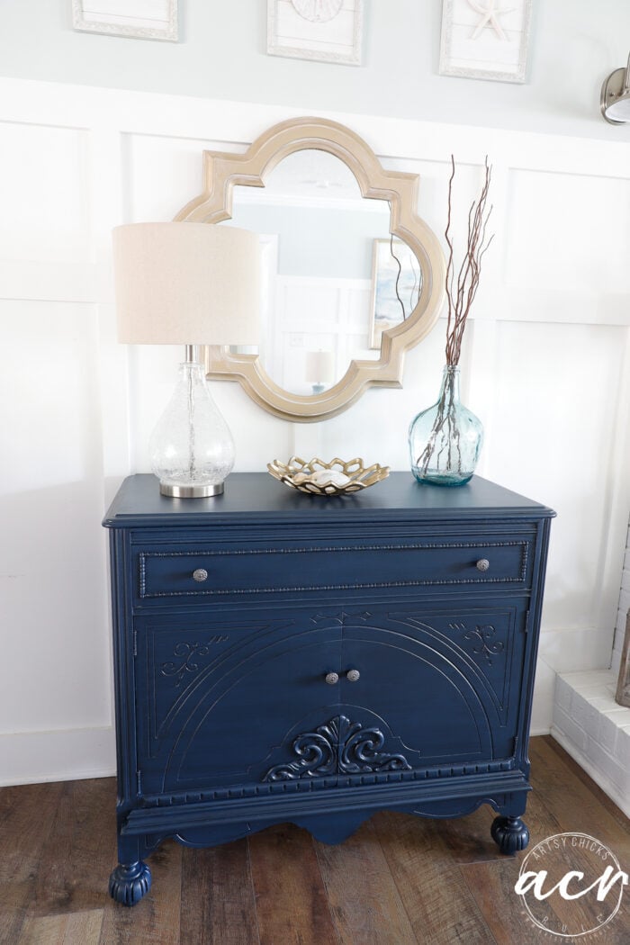 blue cabinet with lamp and aqua glass vase, gold dish and gold mirror