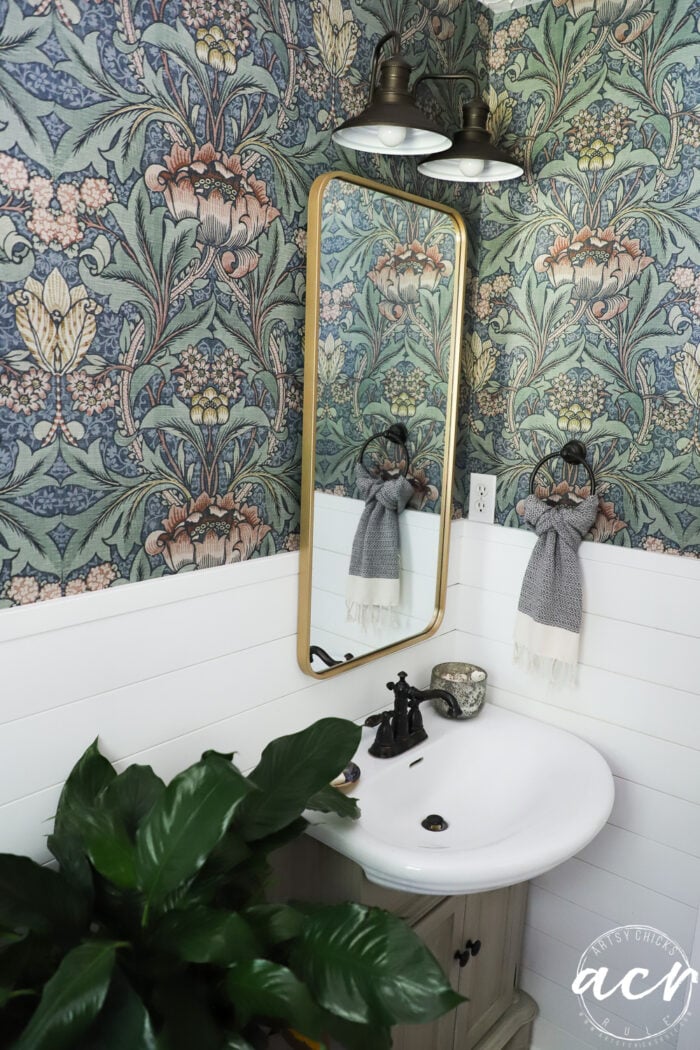 wallpapered wall with gold trim mirror over sink