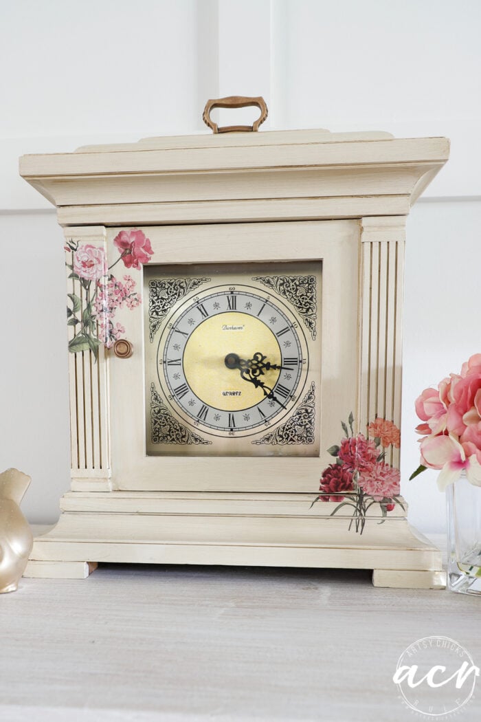front view of mantel clock with glass vase of pink flowers and gold bird decor