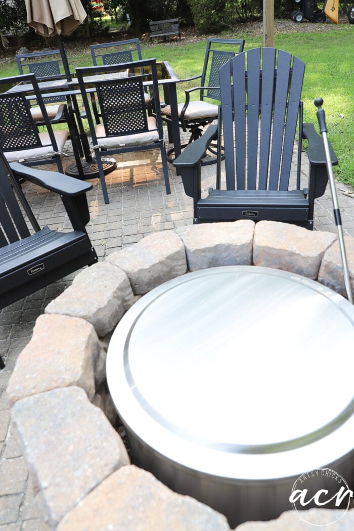 stone and metal firepit with black adirondack chairs