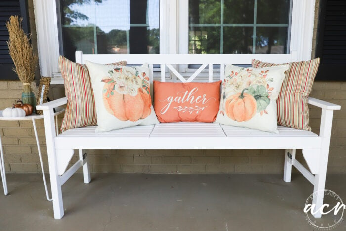 white bench with orange and rust colored pillows. Pumpkin and striped pillows