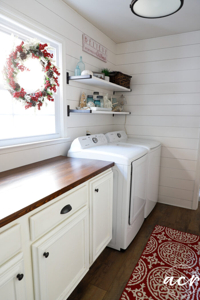 red and white berry wreath on window with shelves and red rug in laundry room