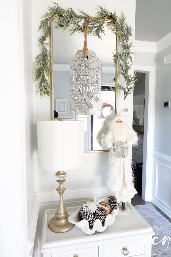 foyer table with white clothed santa, greenery over mirror