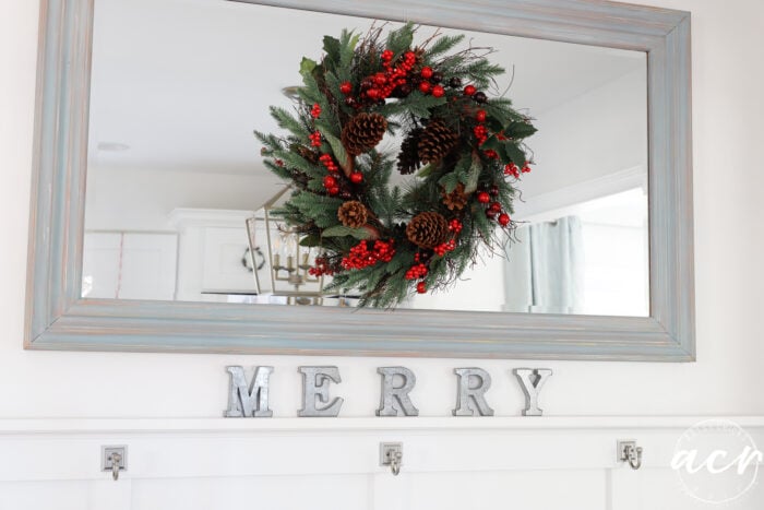mirror with wreath and tin letters below that spell merry