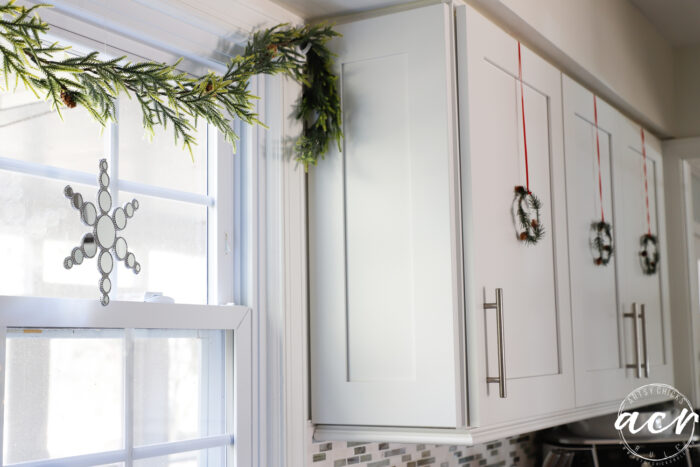 greenery over window with mirrored star and mini green wreaths hanging on cabinet doors