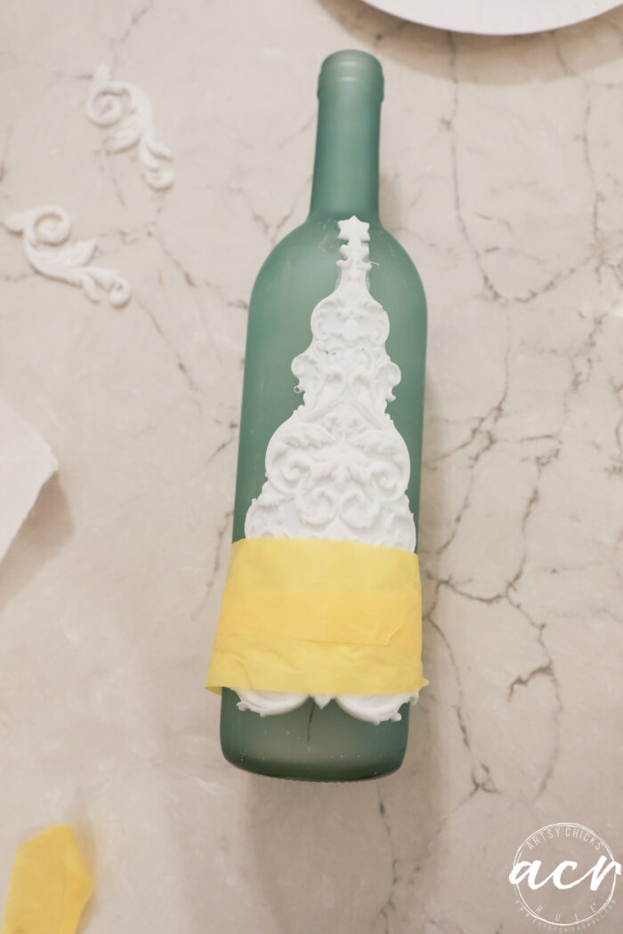 green bottle with white tree taped to front