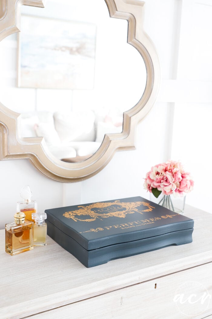 gold mirror on wall with blue flatware box, pink flowers and gold colored perfumes