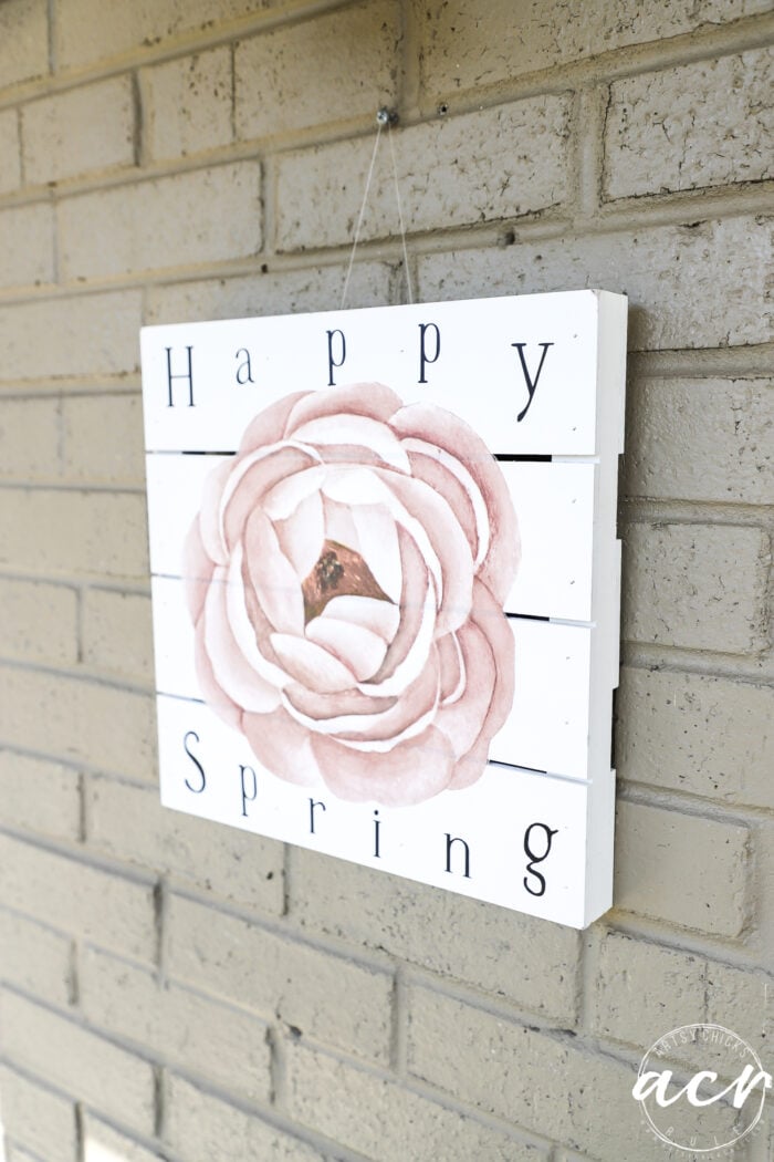 happy spring sign hanging on brick wall of front porch