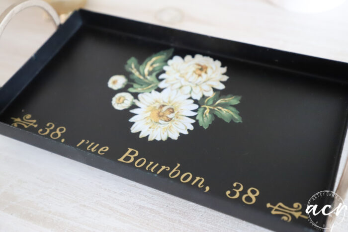 gold and black tray with white floral and gold lettering