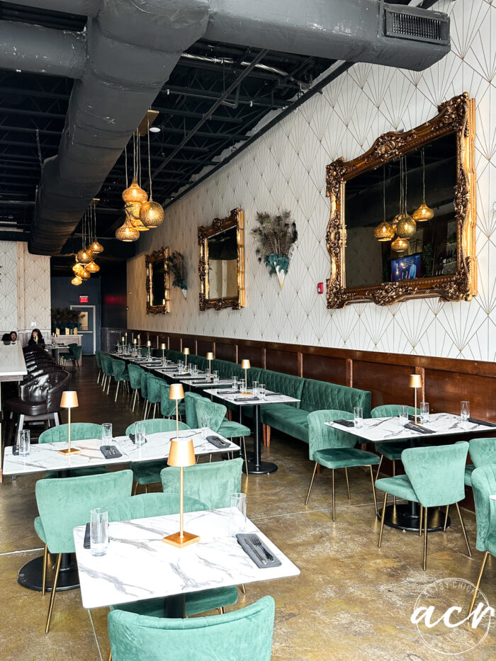beautiful restaurant with aqua velvet chairs, huge ornate gold mirrors along the wall, gold floor, marble tables, black ceiling