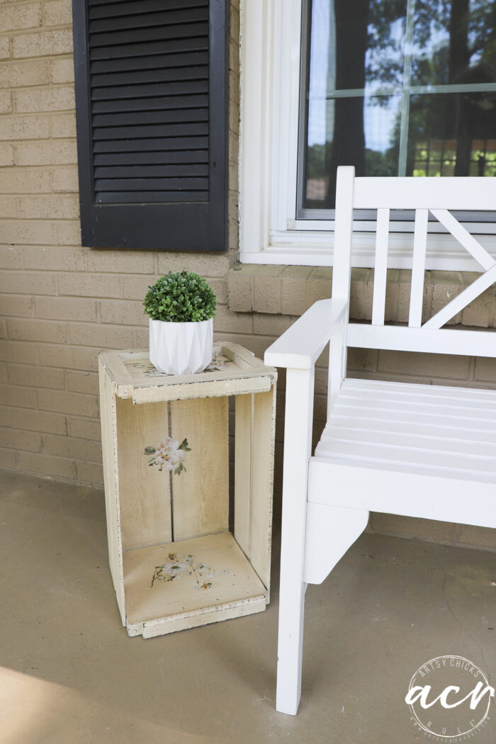 crate standing tall beside white bench with small green plant on top