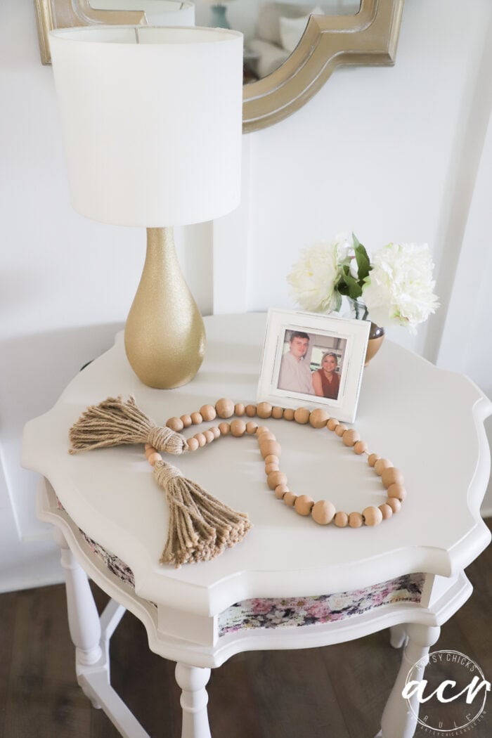 top of styled table with framed photo, flowers and gold lamp