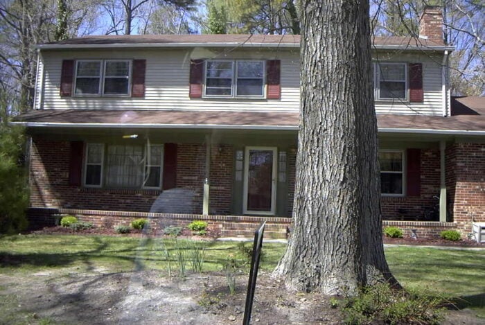 maroon shuttered, green trimmed beige siding with multicolor brick house