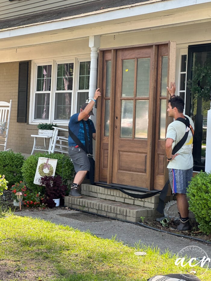 two men holding wood door on front porch