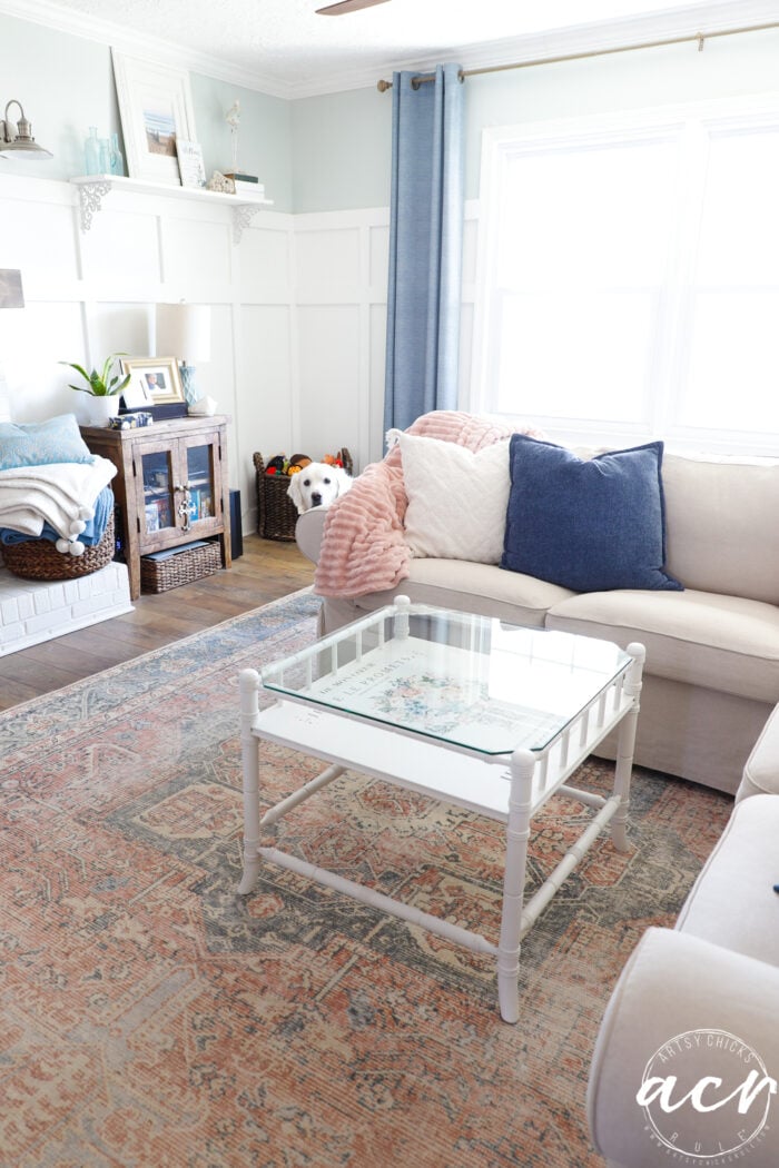 living room with table and white dog peeking around the back of couch