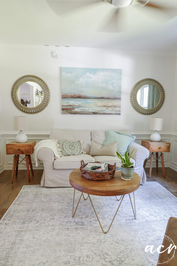 living area with small couch, coffee table, side tables and mirrors with artwork on wall