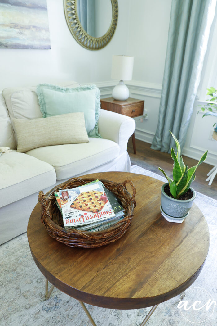 round stained coffee table with basket on top with magazines and green plant