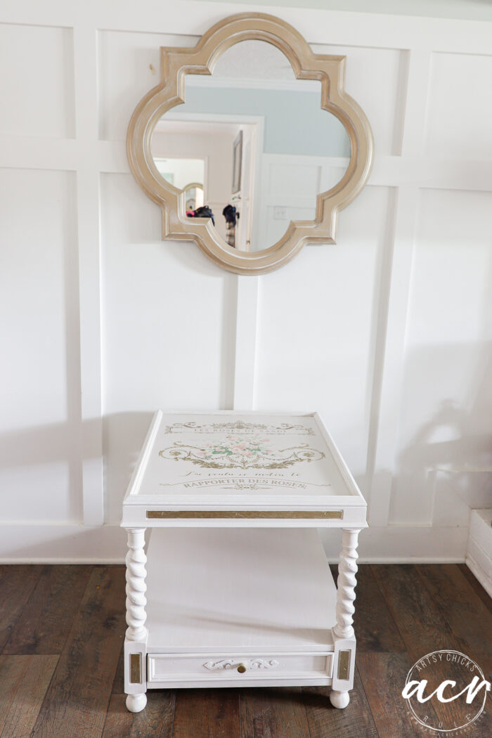 table in front of white wall and under gold mirror