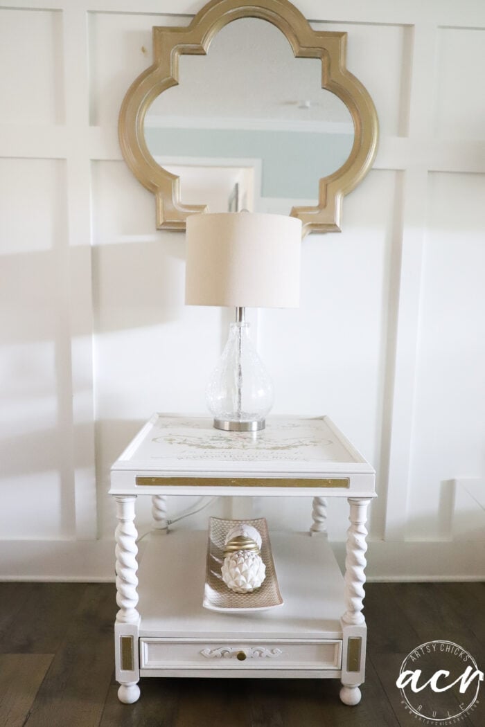 table with clear glass lamp under gold mirror