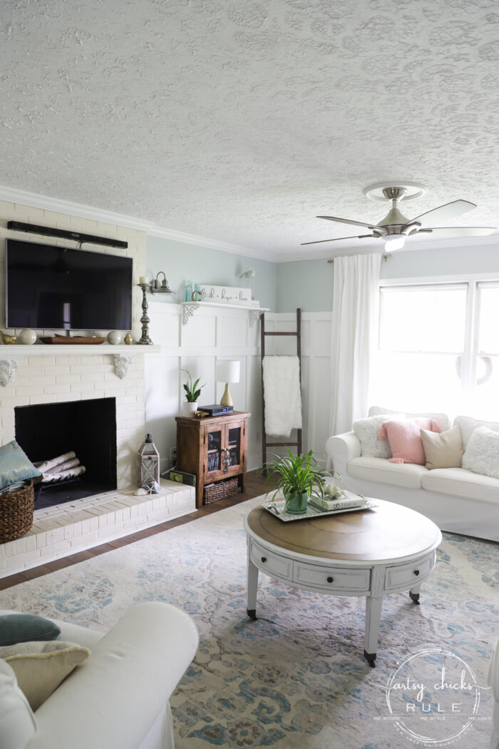 fireplace, round coffee table, white curtains, blue rug, white couch
