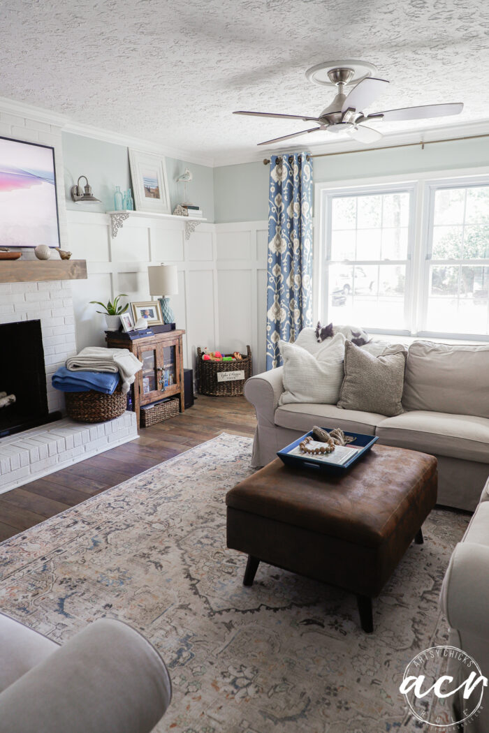 living room with tan furniture, blue curtains brown seude ottoman