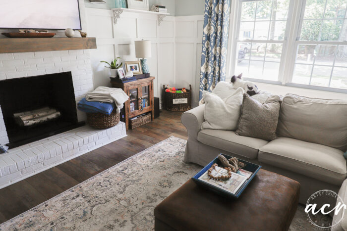 living room with brown, blue, coral multicolor rug, ottoman and tan couch with dog sitting on back