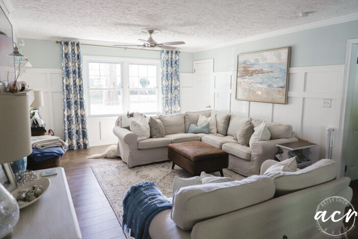 blue patterned curtains, brown tan and blue colored rug, tan furniture, blue and white walls
