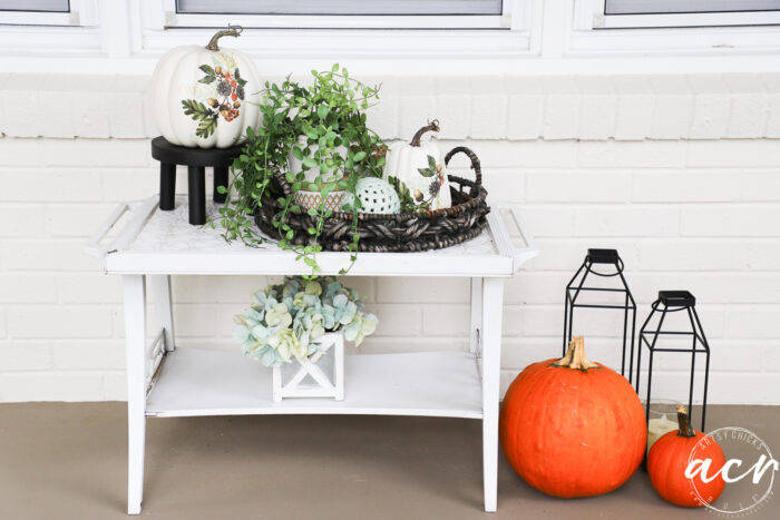 small white table with pumpkins beside and pumpkins on top with decorative design