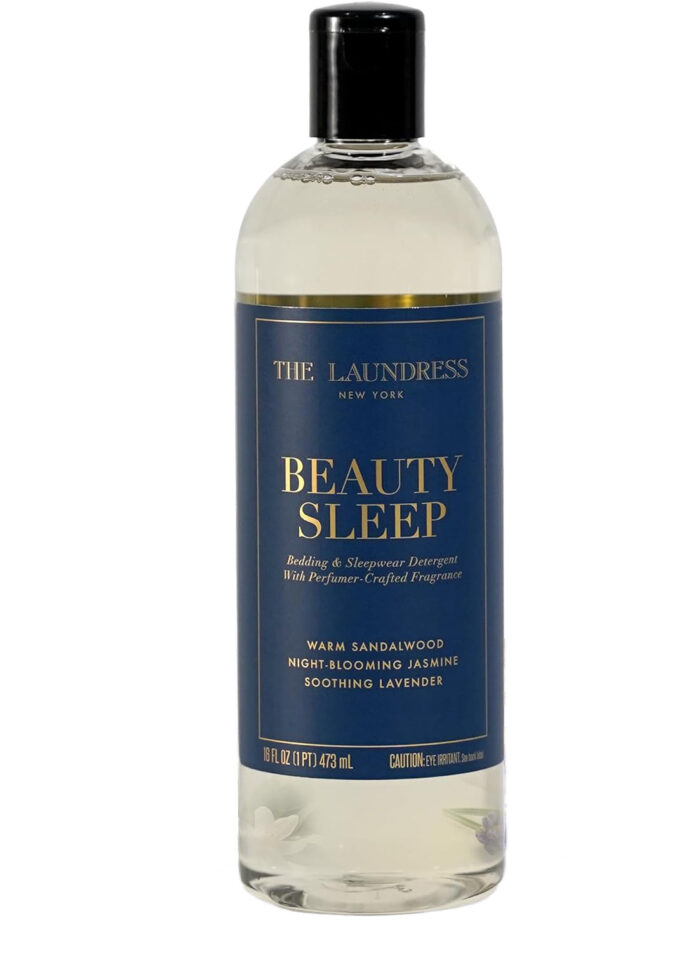 A clear bottle of The Laundress Beauty Sleep detergent with a black cap. The blue label reads, &ldquo;Beauty Sleep: Bedding & Sleepwear Detergent&rdquo;&mdash;an amazon find featuring warm sandalwood, night-blooming jasmine, and soothing lavender.