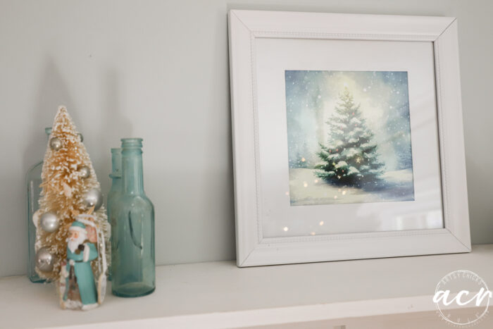 pretty white frame with christmas tree art next to antique blue bottles and small tree