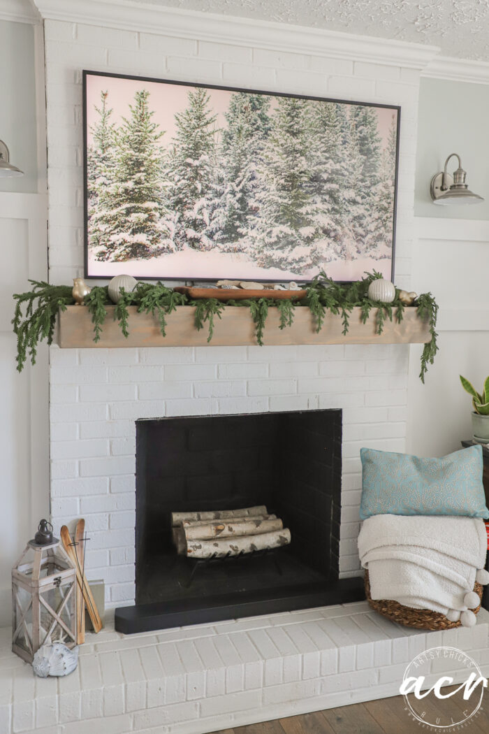 frame tv with green trees and snow on it with greenery on mantel