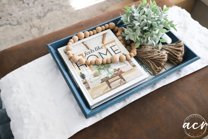 ottoman with white fluffy runner, blue tray with book and green plant