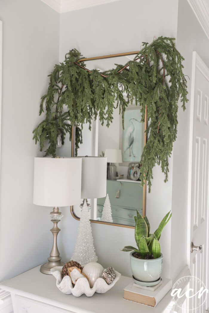 greenery draped over mirror in foyer with white tree and pine cones