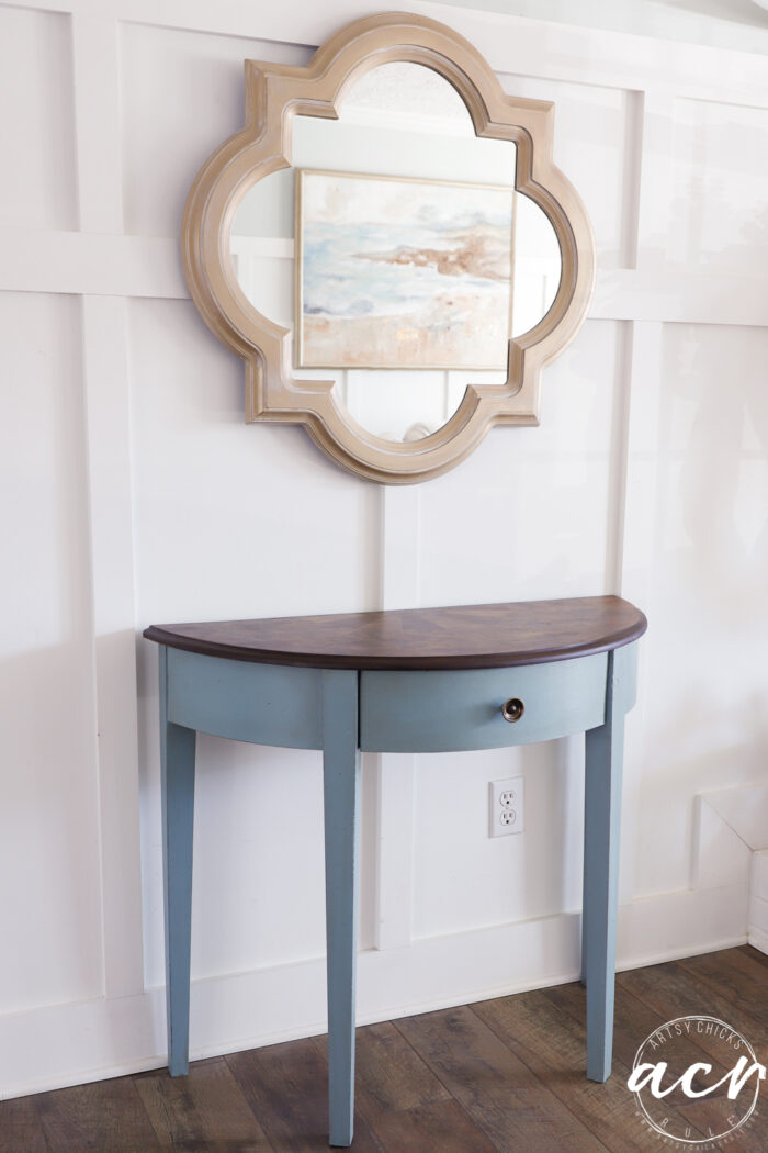 finished blue half moon table with stained top and gold mirror above against white wall