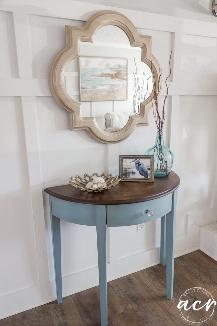 side view of half moon table styled with coastal decor under gold mirror on white wall